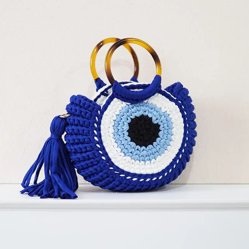 Bolsa Olho Grego azul em crochê sintético, com alça plástica circular, design icônico e toque místico.