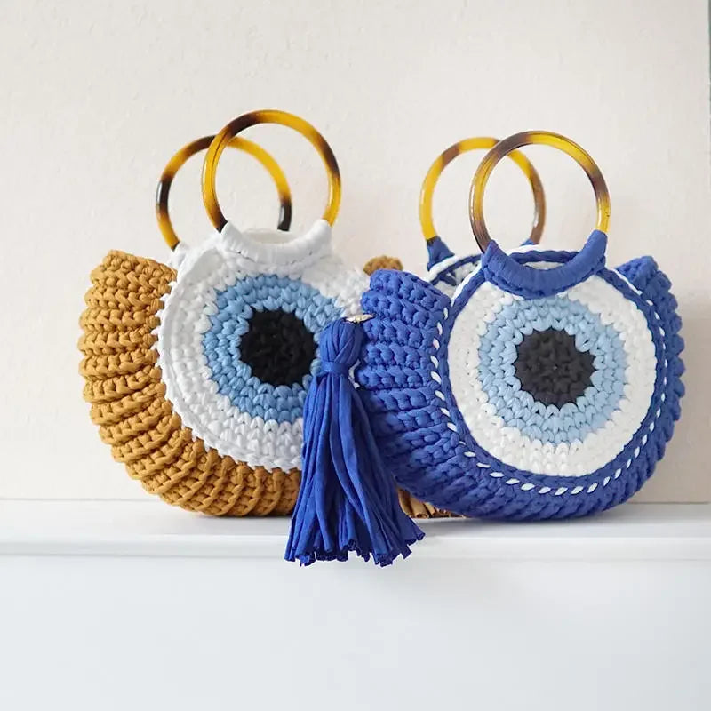 Bolsa Olho Grego em crochê sintético nas cores mostarda e azul, com alça circular plástica e design místico.