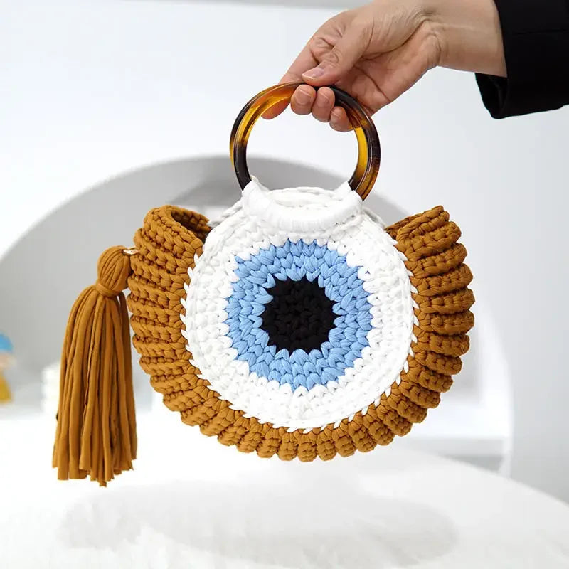 Pessoa segurando bolsa Olho Grego de crochê sintético azul com alça plástica, ideal para compor looks modernos e estilosos
